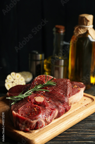 Spices, oil and board with raw steak meat on wooden background