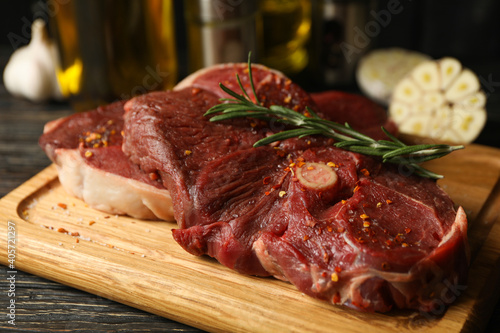Spices, oil and board with raw steak meat on wooden background