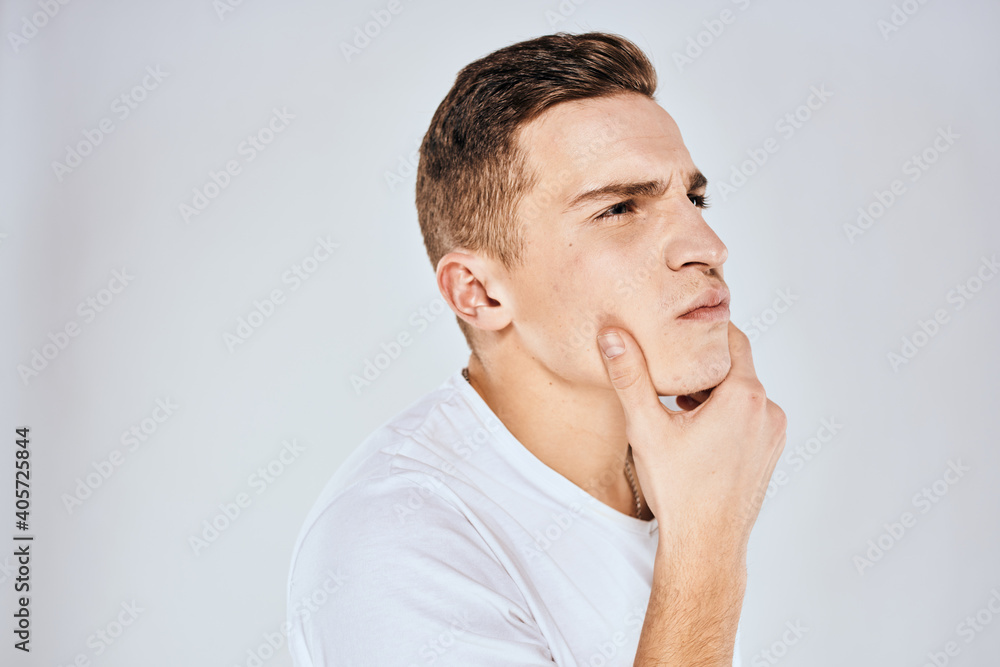 Emotional man in a white t-shirt holds his hand on his face light background