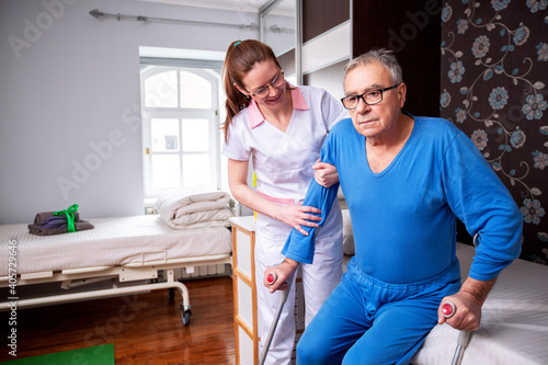Quadro em tela Elder man in nursing home holding a crutch under his arm while nursing home lady