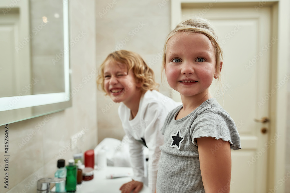 Portrait of cute little girl smiling at camera while washing her face, brushing teeth together with her sibling brother in the bathroom Portrait of cute little girl smiling at camera while washing her face, brushing teeth together with her sibling brother in the bathroom