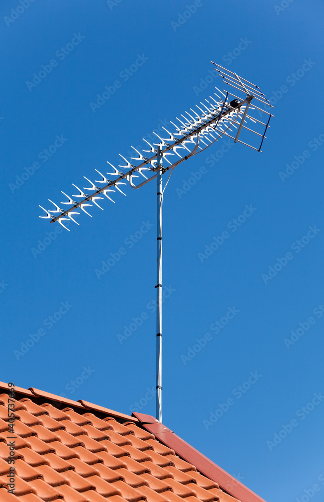 Antenna up on a roof top. Orange brick roof. Clear blue sky. 