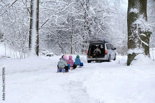 Young children go sledding on a sleigh ride with car along a beautiful snowy road in the forest. 