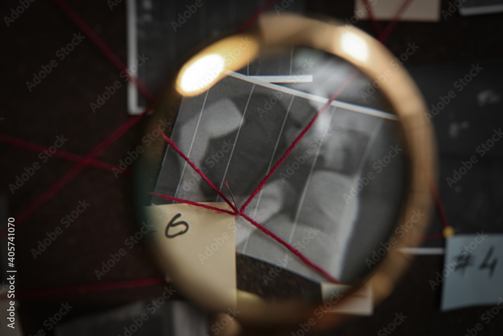 Looking at detective board through magnifying glass, closeup