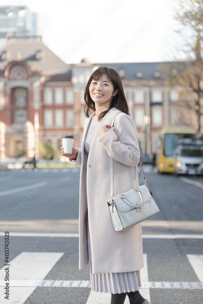 東京駅でコーヒーを持って歩く女性