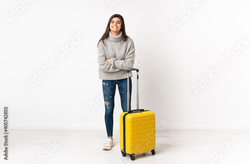 A full length body of a traveler woman with a suitcase over isolated white wall laughing