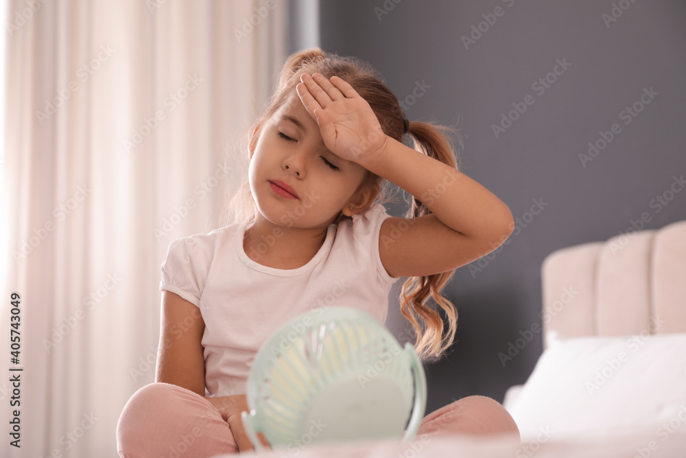 Little girl enjoying air flow from portable fan in room. Summer heat Little girl enjoying air flow from portable fan in room. Summer heat