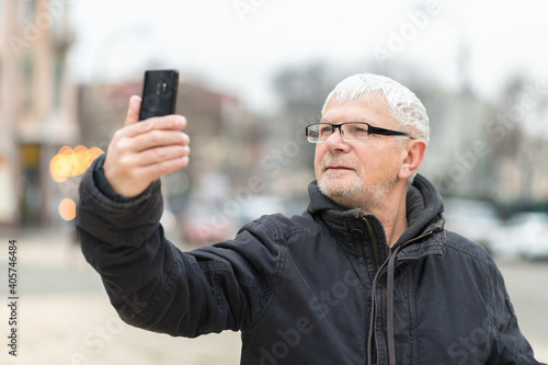 Smiling gray-haired elderly man with a phone in his hand against  backdrop of beautiful city houses