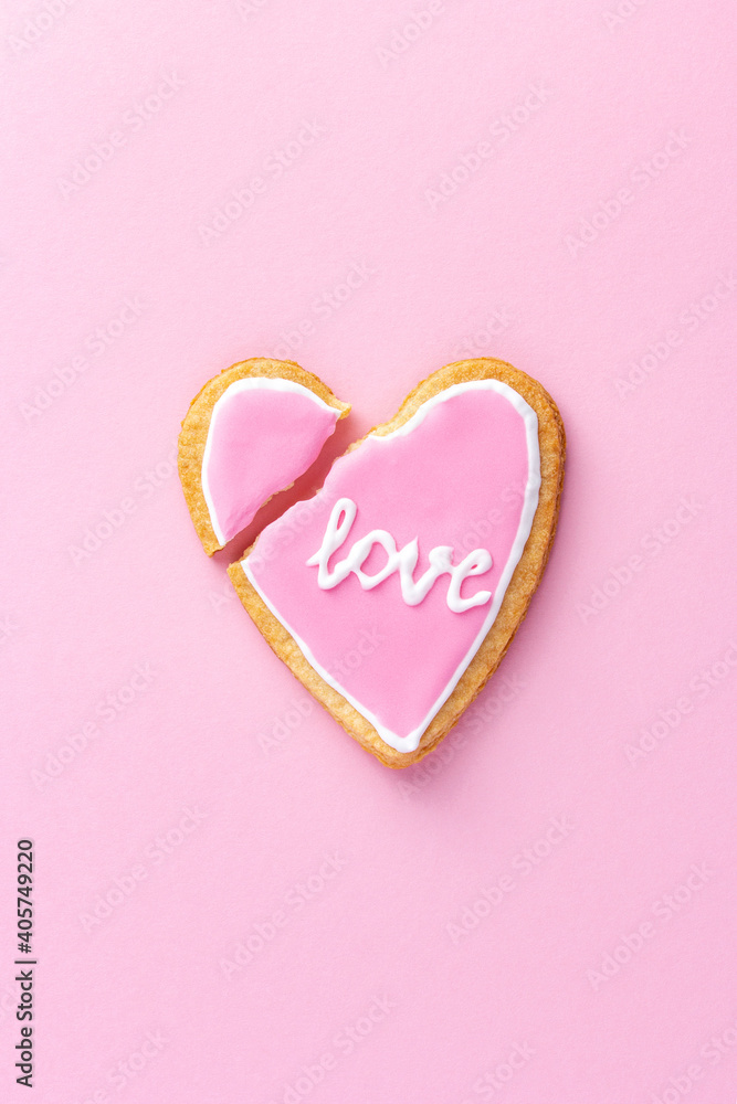 Broken heart shaped cookie with word love on pink background as a symbol of the end of the relationship