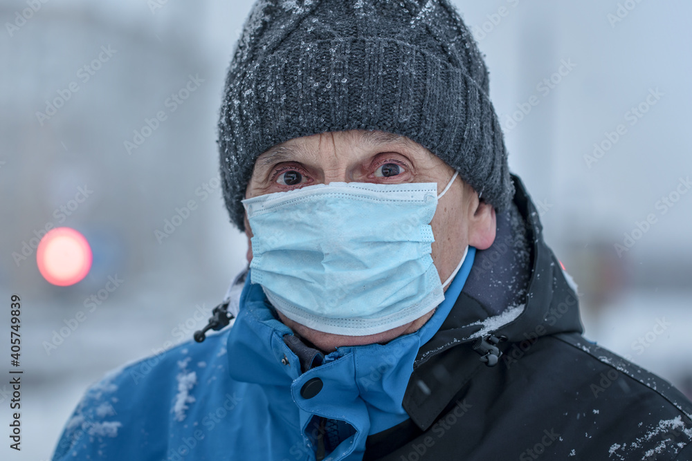Mature sick man in knitted cap and medical face mask at city street