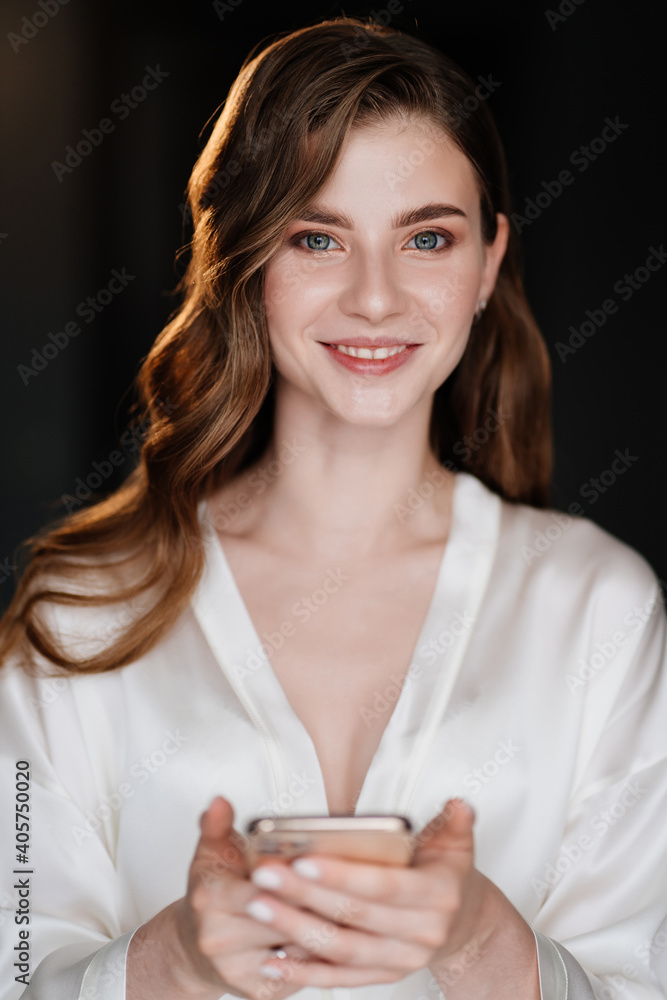 The beautiful woman looks at her photo on the phone with makeup and styling. The beautiful woman looks at her photo on the phone with makeup and styling.