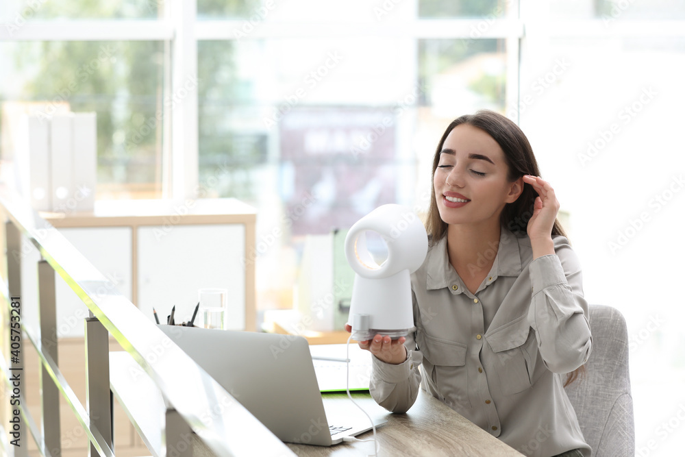 Young woman enjoying air flow from portable fan at workplace, space for text. Summer heat Young woman enjoying air flow from portable fan at workplace, space for text. Summer heat