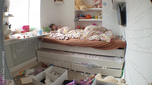 clutter in the children's room, a little girl lies in bed and watches TV in an untidy room