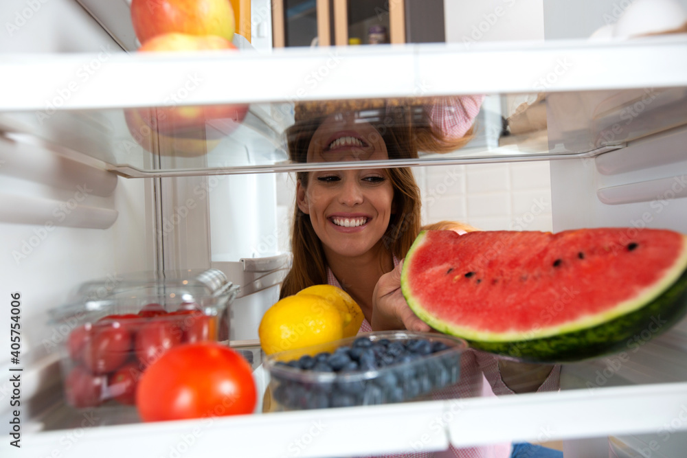 Smiling face lurking between the shelves of a refrigerator full with healthy foods