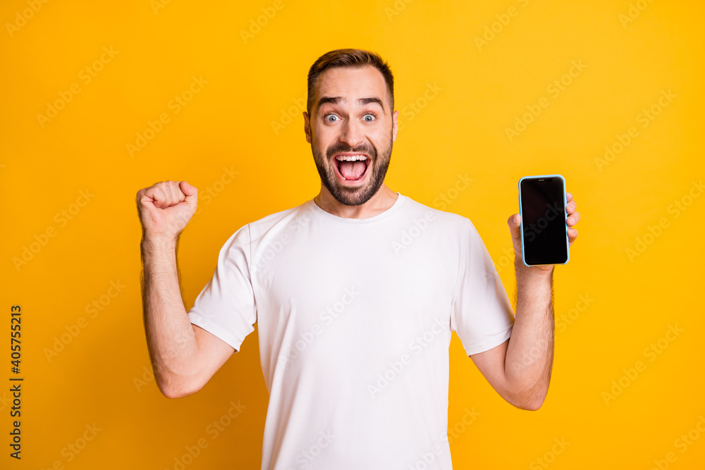 Portrait of attractive cheerful guy holding in hand device celebrating sale having fun isolated over bright yellow color background Portrait of attractive cheerful guy holding in hand device celebrating sale having fun isolated over bright yellow color background