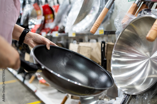 Hands of girl holding a new pan,choosing black teflon frying pan,asian  customer deciding to buy non-stick frying pan for cooking food in her kitchen,shopping cookware household goods at supermarket