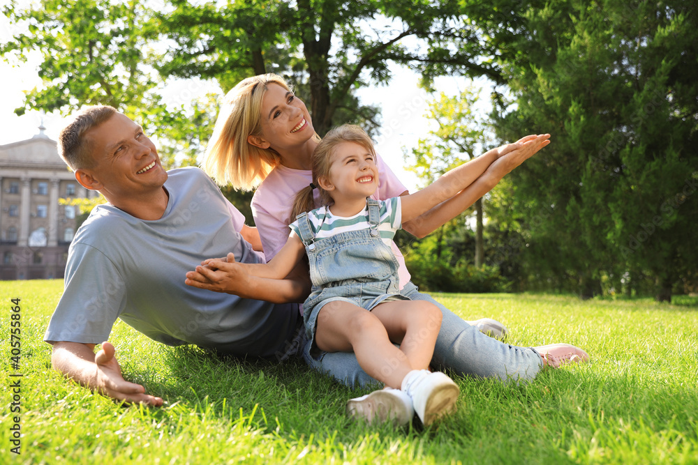Fototapeta premium Happy parents with their child having fun on green grass. Spending time in nature