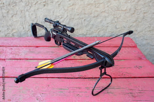 Fotografi A modern crossbow with arrows and an optical sight lies on a wooden table in the