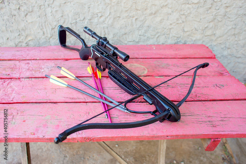 Fotografie A modern crossbow with arrows and an optical sight lies on a wooden table in the