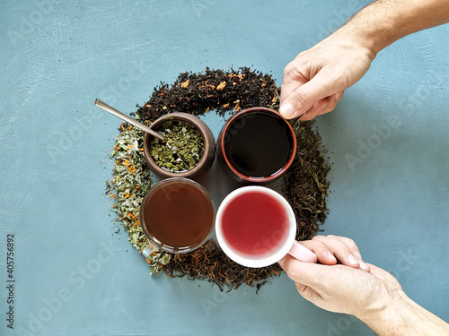 4 mugs with different types of tea and hands picking 2 cups photo