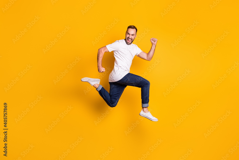 Full length body size photo of jumping cheerful male model wearing stylish outfit isolated vivid yellow color background