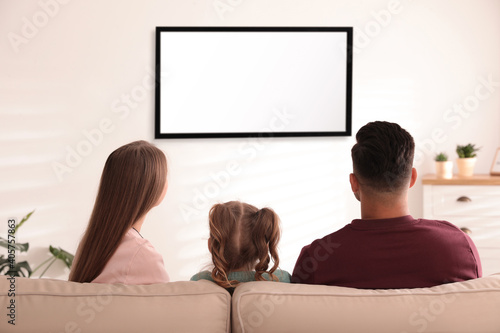 Family watching TV on sofa at home, back view