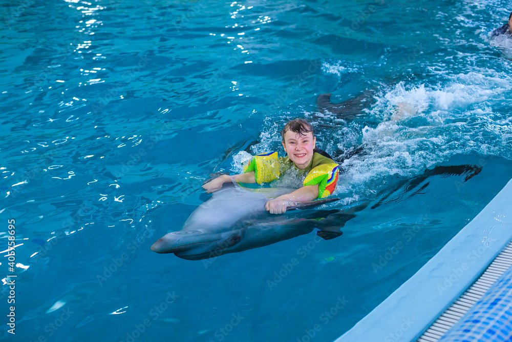 Treatment of children by means of dolphins. Dolphin therapy. Happy little girl swimming with dolphins in Dolphinarium. Swimming, bathing and communication with dolphins. Concept People and dolphins.
