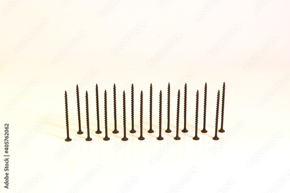 Self-tapping screws for wood surfaces, standing on hats, on a light background. Components for construction and repair. Metal fasteners. Self-tapping screws for wood surfaces, standing on hats, on a light background. Components for construction and repair. Metal fasteners.
