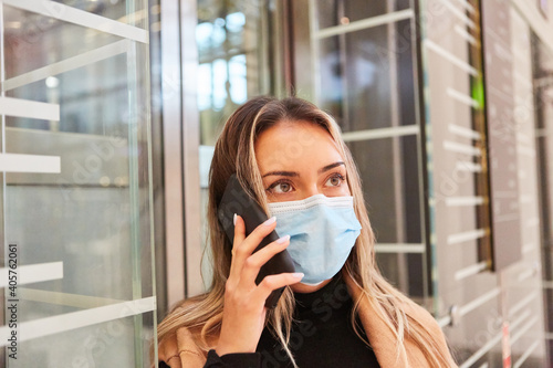 Junge Frau mit Mundschutz telefoniert mit Smartphone