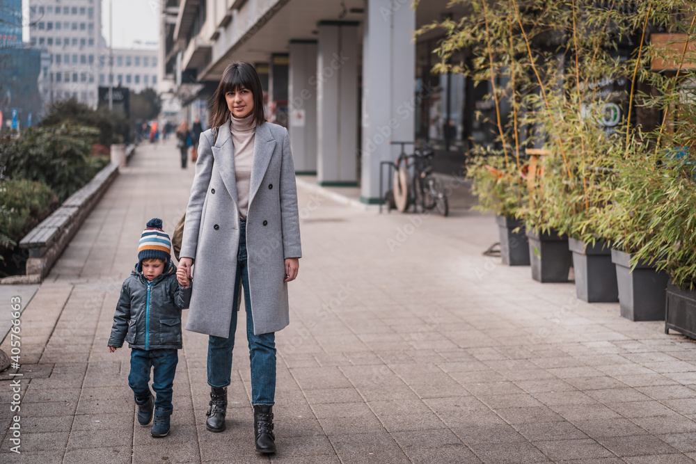 Beautiful happy young mom with her adorable little kid son walking in city