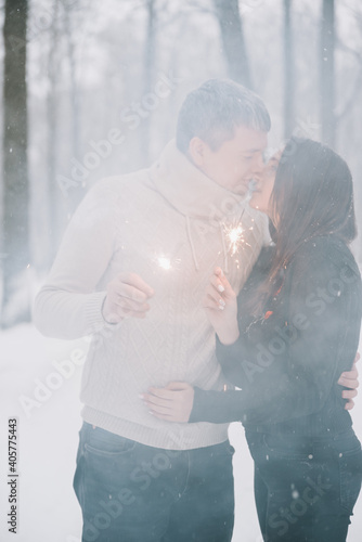 A man and a woman with sparklers on the background of a snow-covered forest in a snowfall