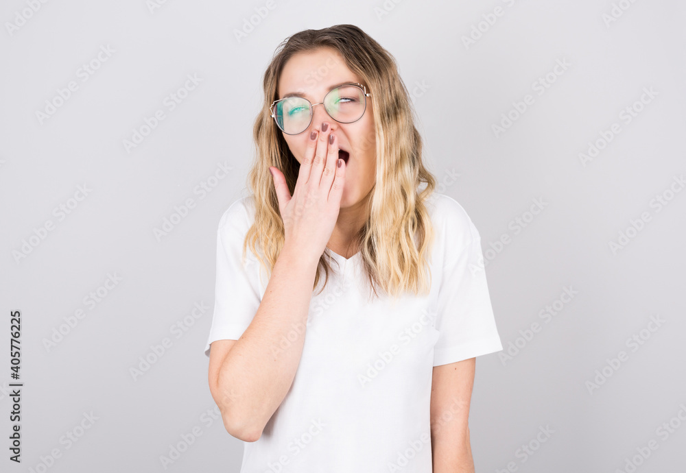 Young woman with disheveled hair yawns from fatigue against gray wall Young woman with disheveled hair yawns from fatigue against gray wall
