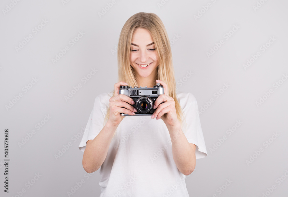Expressive portrait of a beautiful young blonde woman in a white T-shirt in the studio on a gray background with a camera in her hands Expressive portrait of a beautiful young blonde woman in a white T-shirt in the studio on a gray background with a camera in her hands