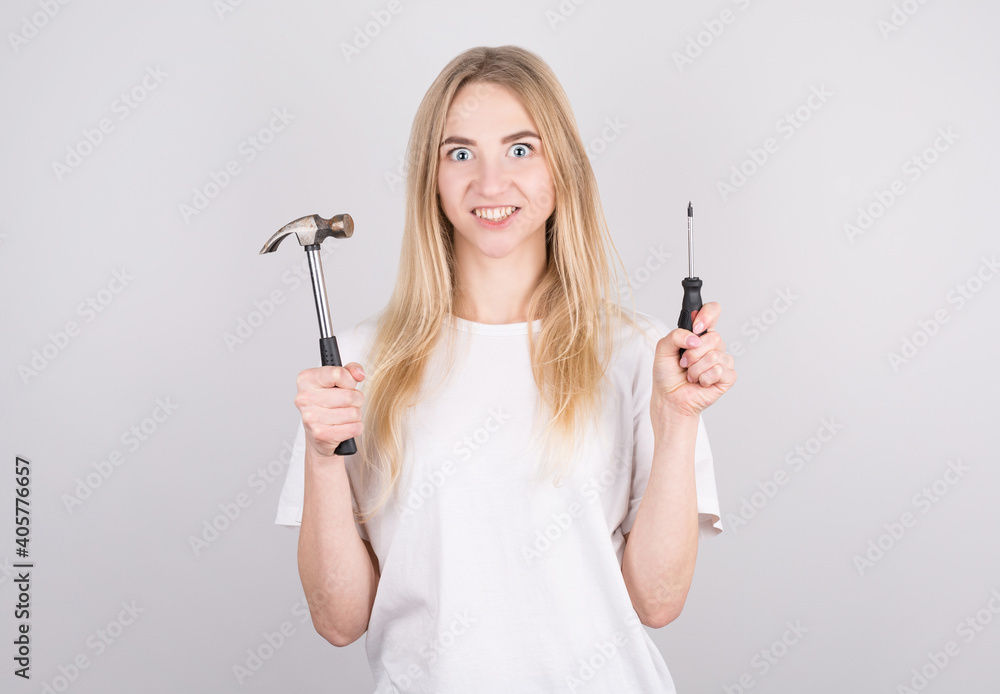 The girl holds a hammer and a screwdriver and looks scared, not understanding what to do with it and how The girl holds a hammer and a screwdriver and looks scared, not understanding what to do with it and how