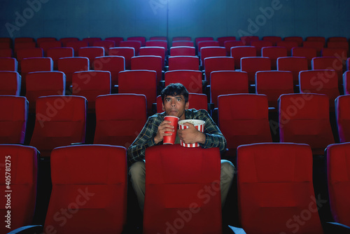 Billede på lærred Focused young man holding a drink and popcorn basket while watching movie alone
