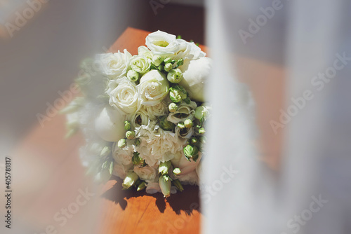 a delicate bridal bouquet of white flowers on the windowsill. view through the curtains. morning of the bride