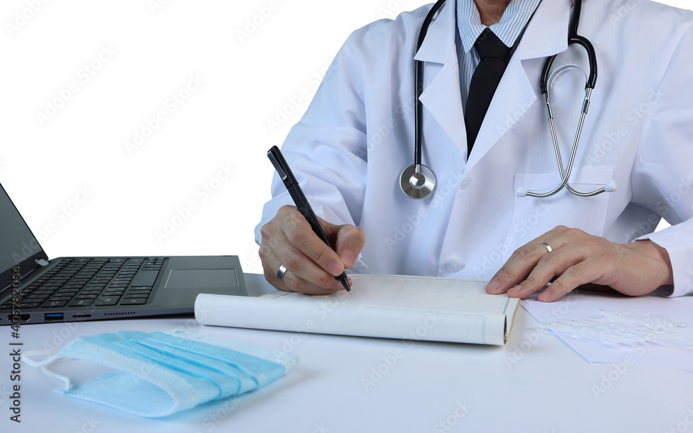 doctor with stethoscope is writing on the notebook while working examine patient on white table with laptop computer , mask and some medecines in the hospital clinic isolated on white wall background doctor with stethoscope is writing on the notebook while working examine patient on white table with laptop computer , mask and some medecines in the hospital clinic isolated on white wall background