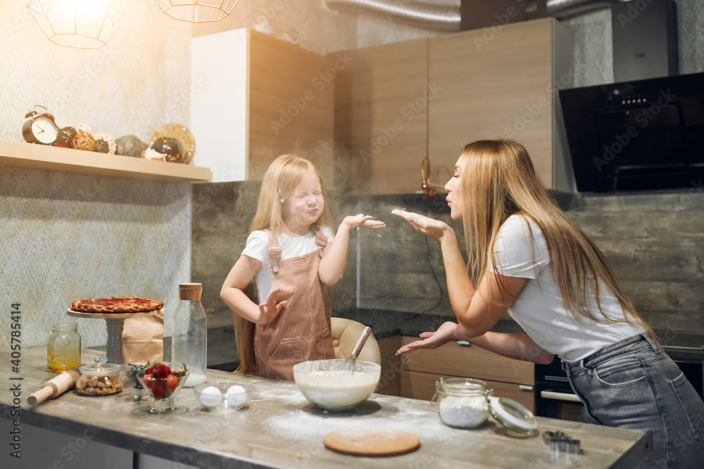 Mother and daughter are preparing pancakes. Family cooking. Preparing breakfast. Knead the dough. Soiled in flour, hug each other Mother and daughter are preparing pancakes. Family cooking. Preparing breakfast. Knead the dough. Soiled in flour, hug each other