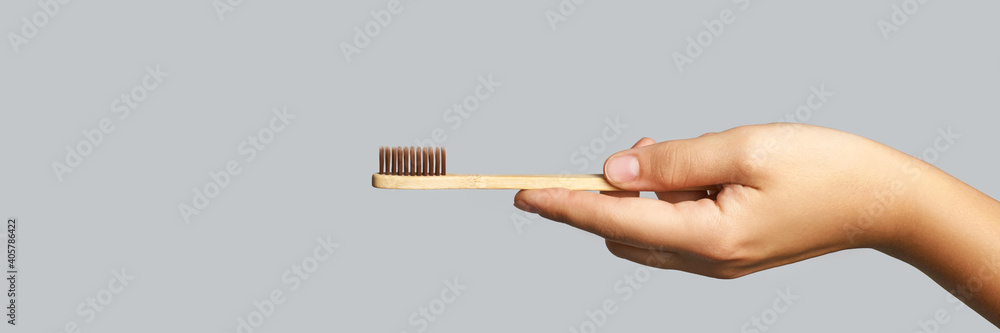 Hand holding toothbrush. Bamboo eco brush. Dental sustainable concept. Layout. Morning home routine. Grey background. Medicine cosmetics. Mouth hygiene treatment. Personal cleaning. Copyspace, banner Hand holding toothbrush. Bamboo eco brush. Dental sustainable concept. Layout. Morning home routine. Grey background. Medicine cosmetics. Mouth hygiene treatment. Personal cleaning. Copyspace, banner
