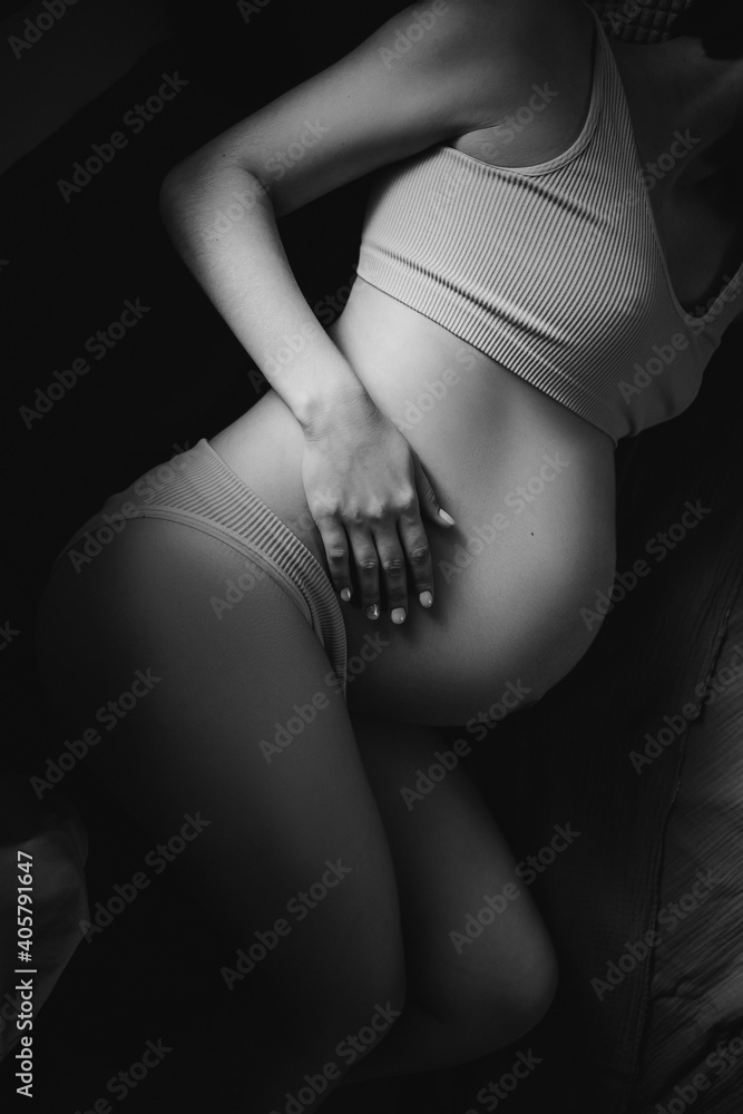 Black and white frame of a young pregnant girl in underwear lies on her side on the floor in the bedroom