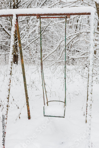 Fototapeta Naklejka Na Ścianę i Meble -  Stara, metalowa huśtawka ustawiona w środku lasu w zimowej śnieżej białej scenerii