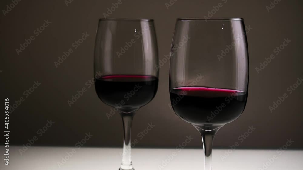 Red wine, in two glasses on a table against a dark background. Slow motion medium shot. Red wine, in two glasses on a table against a dark background. Slow motion medium shot.