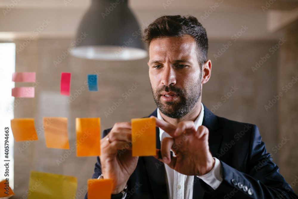 Businessman in conference room use sticky notes on glass wall. Handsome businessman making a business plan..