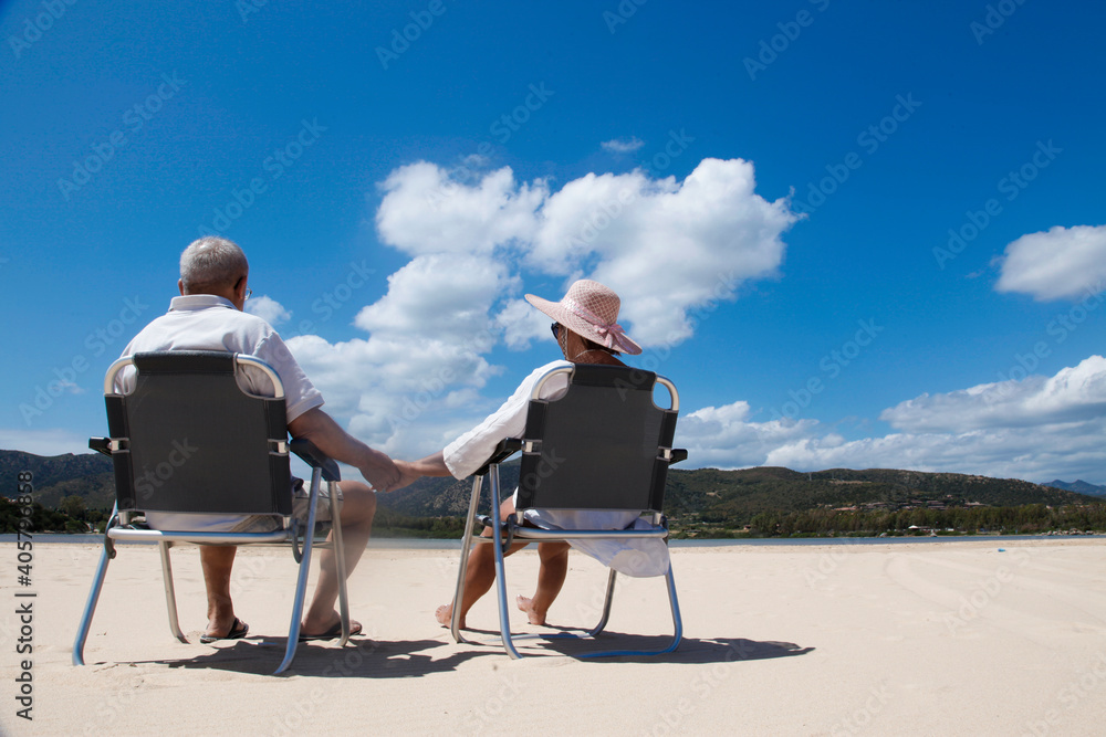 coppia di anziani si tiene teneramente la mano seduti in una sedia in spiaggia