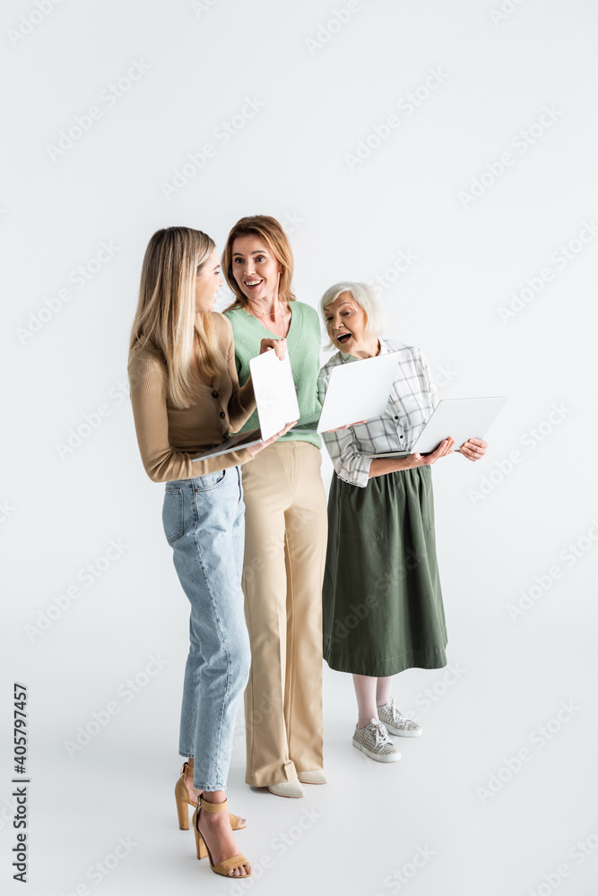 full length of three generation of women holding laptops and smiling on white full length of three generation of women holding laptops and smiling on white
