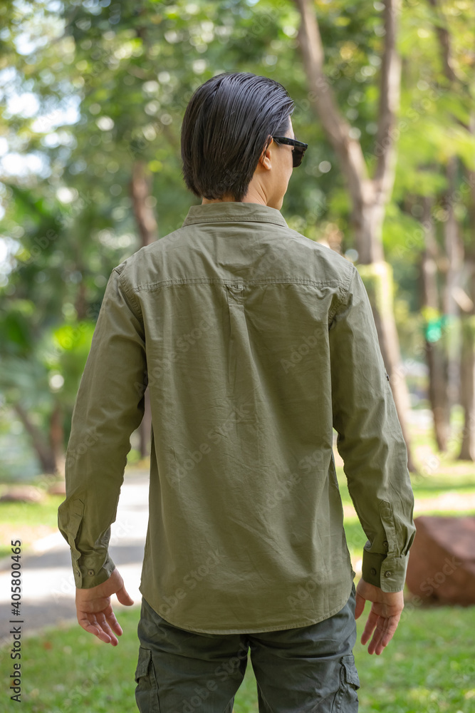 Portrait of happy asian young man in long sleeve shirt and green pant standing in the park Portrait of happy asian young man in long sleeve shirt and green pant standing in the park