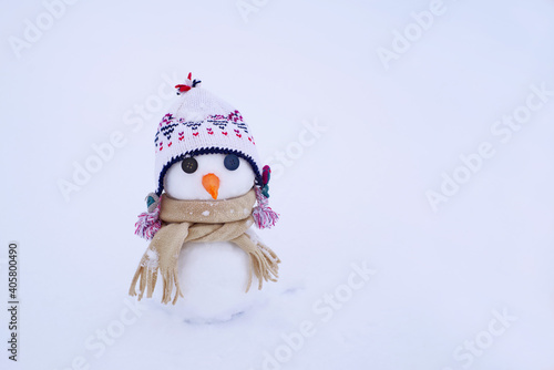 Little cute snowman in a hat and a scarf with a carrot nose on the snow on a winter day, close-up. Holiday card with a snowman