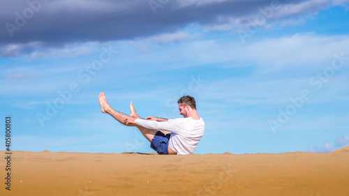 Young man falling and laughing on the sand in dunes in Gran Canaria