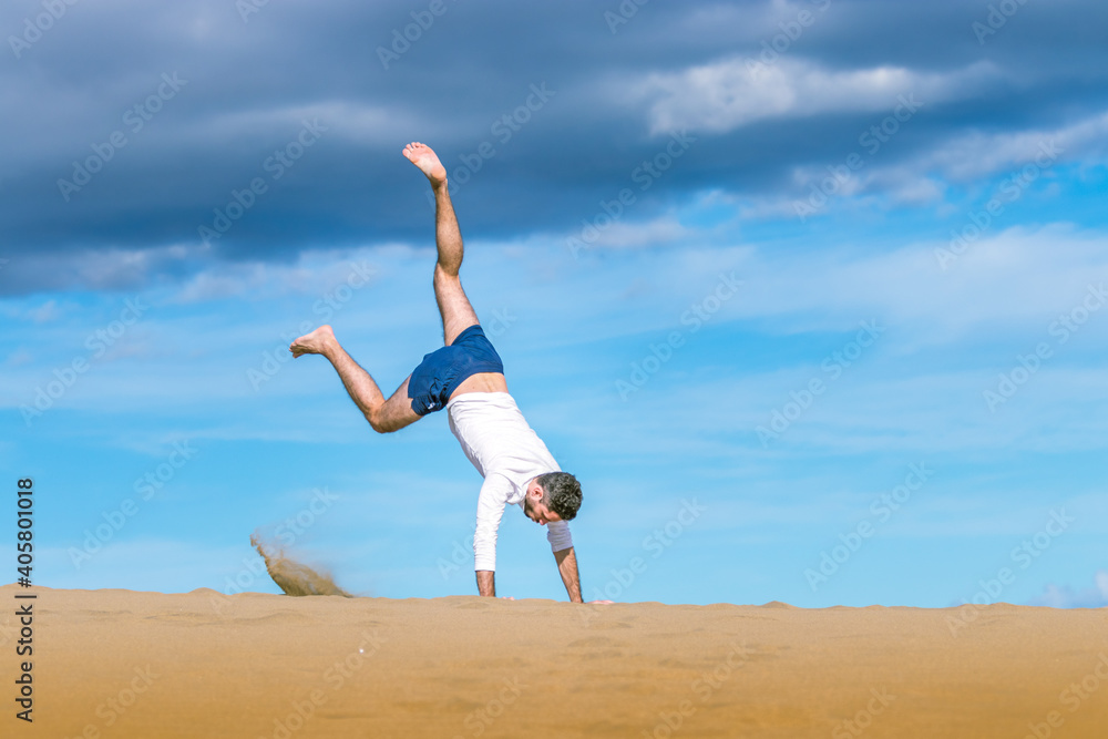 Athletic young man doing acrobatics in the sand of the dunes in Gran Canaria Athletic young man doing acrobatics in the sand of the dunes in Gran Canaria