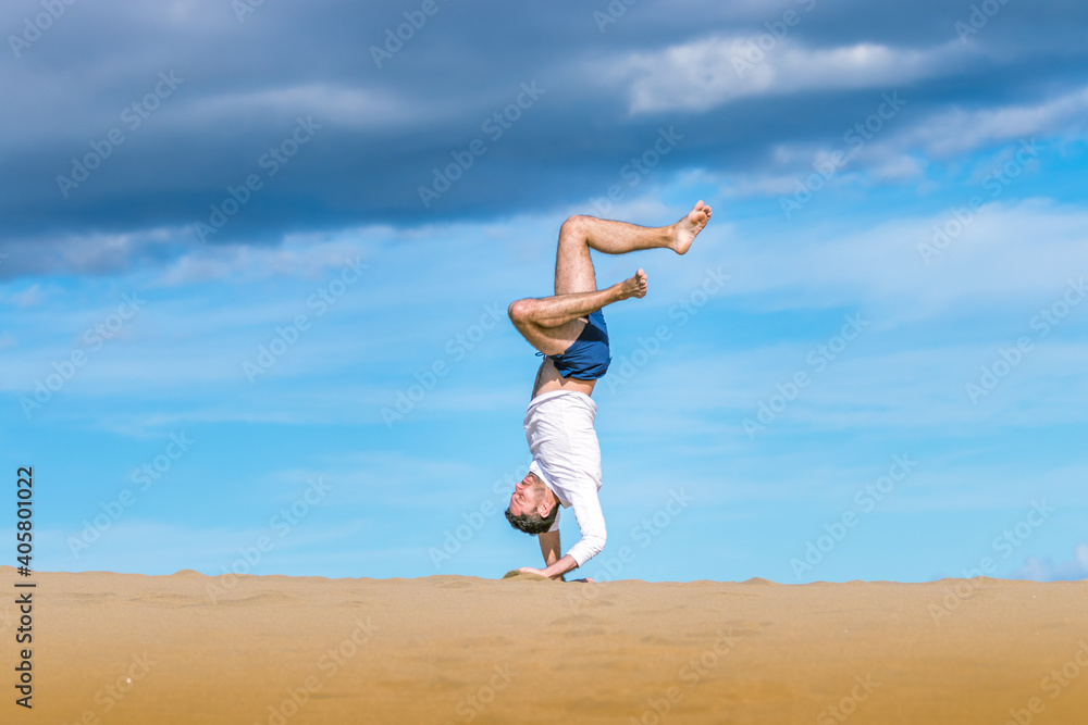 Athletic young man doing acrobatics in the sand of the dunes in Gran Canaria Athletic young man doing acrobatics in the sand of the dunes in Gran Canaria